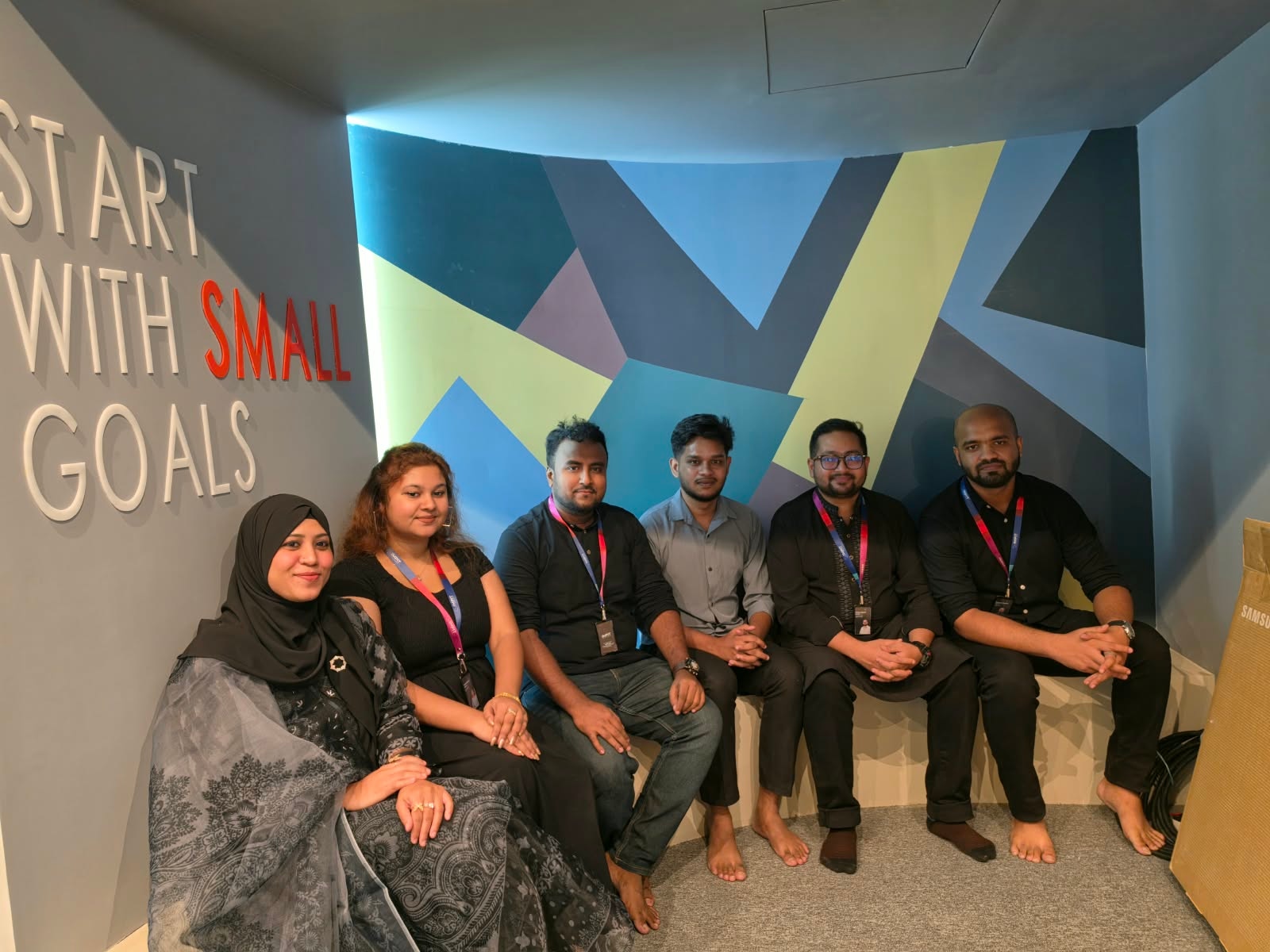 IMPIT team seated in front of the Start With Small Goals wall